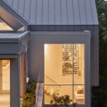 Pohľad na schodisko cez presklenú stenu s osvetlenou vinotékou, béžovou sedacou nikou.modernej architektúry.