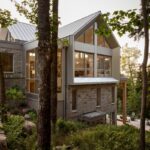 Horská rezidencia s výrazným štítom, svetlým kamenným obkladom a hliníkovými okennými rámami v obklopení stromov.