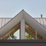 Štít sedlovej strechy so sivou plechovou krytinou, integrovanými trojuholníkovými oknami a kovovým komínom.