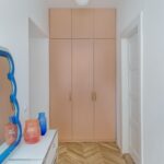 Matná marhuľová šatníková skriňa v úzkej chodbe so zrkadlom v modrom vlnitom ráme.