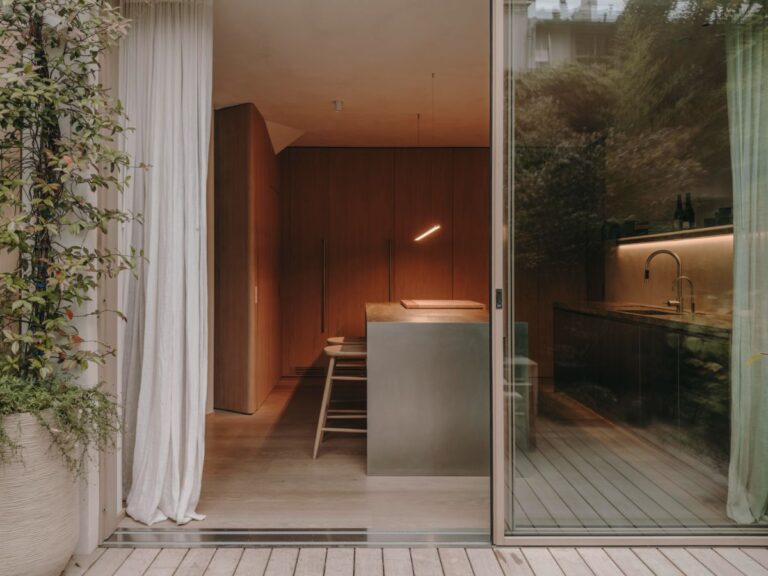 Pohľad do kuchyne s nerezovým ostrovom, drevenými barovými stoličkami, vysokými skriňami z dubovej dyhy a preskleným vstupom na terasu.