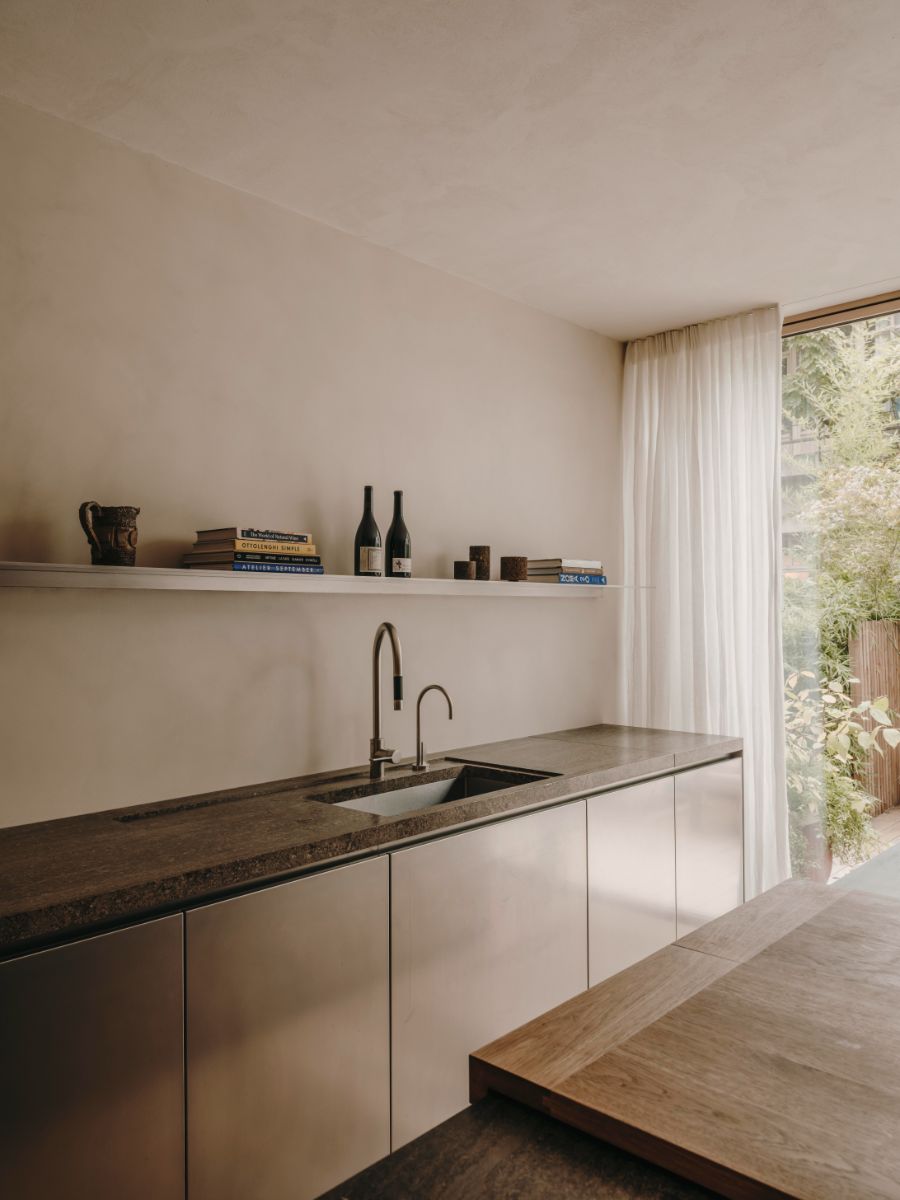 Kuchyňa s kamennou pracovnou doskou, nerezovými skrinkami, dizajnovou batériou, bielou policou a ľanovými závesmi.