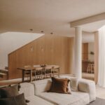 Obývacia izba so svetlou modulárnou pohovkou, jedálenským kútom v pozadí a dreveným obkladom schodiska.