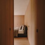 Pohľad do spálne so vstavaným dreveným šatníkom, dubovou podlahou a pohľadom do spálne na posteľ s hnedým čelom.