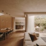 Obývacia izba s béžovou sedačkou, dlhým jedálenským stolom, bielym stĺpom a výhľadom cez veľkoformátové okno do záhrady.