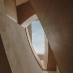 Pohľad do stropu chodby s drevenými a betónovými panelmi, podhľadovými sklami a výhľadom na oblohu.