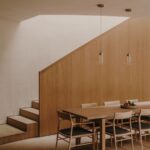 Jedáleň s moderným jedálenským stolom, dubovými stoličkami, čiernymi sedákmi, dreveným schodiskom a stropnými lampami.