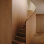 Chodba s dreveným schodiskom, obkladom stien, podlahou z dreva a skrytými dverami.