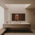 Kúpeľňa s umývadlom a skrinkou z travertínu, zrkadlom s dreveným rámom, ľanovými závesmi a stropným oknom.