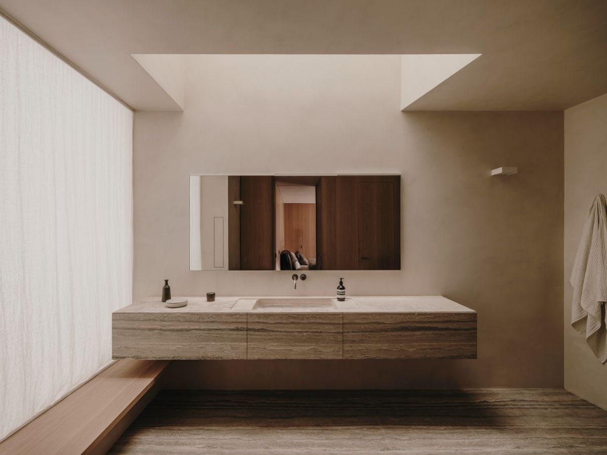 Kúpeľňa s umývadlom a skrinkou z travertínu, zrkadlom s dreveným rámom, ľanovými závesmi a stropným oknom.