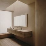 Kúpeľňa s travertínovým umývadlom, skrinkou, zrkadlom, ľanovými závesmi a stropným oknom.