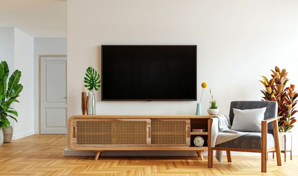 Televízia nad nízkou skrinkou s posuvnými dverami s ratanovým výpletom v obývačke.