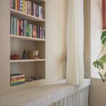 Polica s knihami s posuvnými preglejkovými dvermi a zaťahovacím závesom.