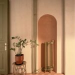 Úzka tehlová oblúková nika s olivovým radiátorom, terakotová dlažba, prútený stojan s kvetom a olivové kazetové dvere.