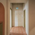 Chodba s terakotovou podlahou, zelenými zárubňami a modrým guľatým svietidlom v minimalistickom štýle.