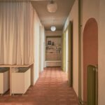 Chodba s terakotovou dlažbou, otvorenými policami, zelenými zárubňami a klenbovým výklenkom v korálovej farbe.