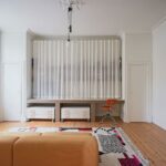 Pracovný kút v obývačke so stolom obloženým kachličkami a otvorenými policami, skrytými za bielymi záclonami.