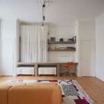 Pracovný kút v obývačke so stolom obloženým kachličkami a otvorenými policami, skrytými za bielymi záclonami.