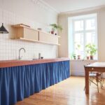 Kuchyňa s linkou s tehlovým obkladom pracovnej dosky, modrým závesom a dreveným jedálenským stolom.