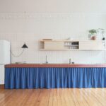 Kuchyňa s lineárnou linkou s tehlovým obkladom pracovnej dosky, modrým závesom a policou s posuvnými dverami.