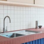 Kuchyňa s nerezovým drezom, pákovou batériou, tehlovým obkladom pracovnej dosky a bielymi štvorcovými kachličkami.