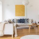 Svetlá rohová sedačka, žltý abstraktný obraz, drevený konferenčný stolík a biela tehlová obstavba krbu.