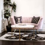 Ružová zamatová pohovka, čierne vzorované vankúše, mramorový stolík so zlatou podnožou a vysoký fikus.