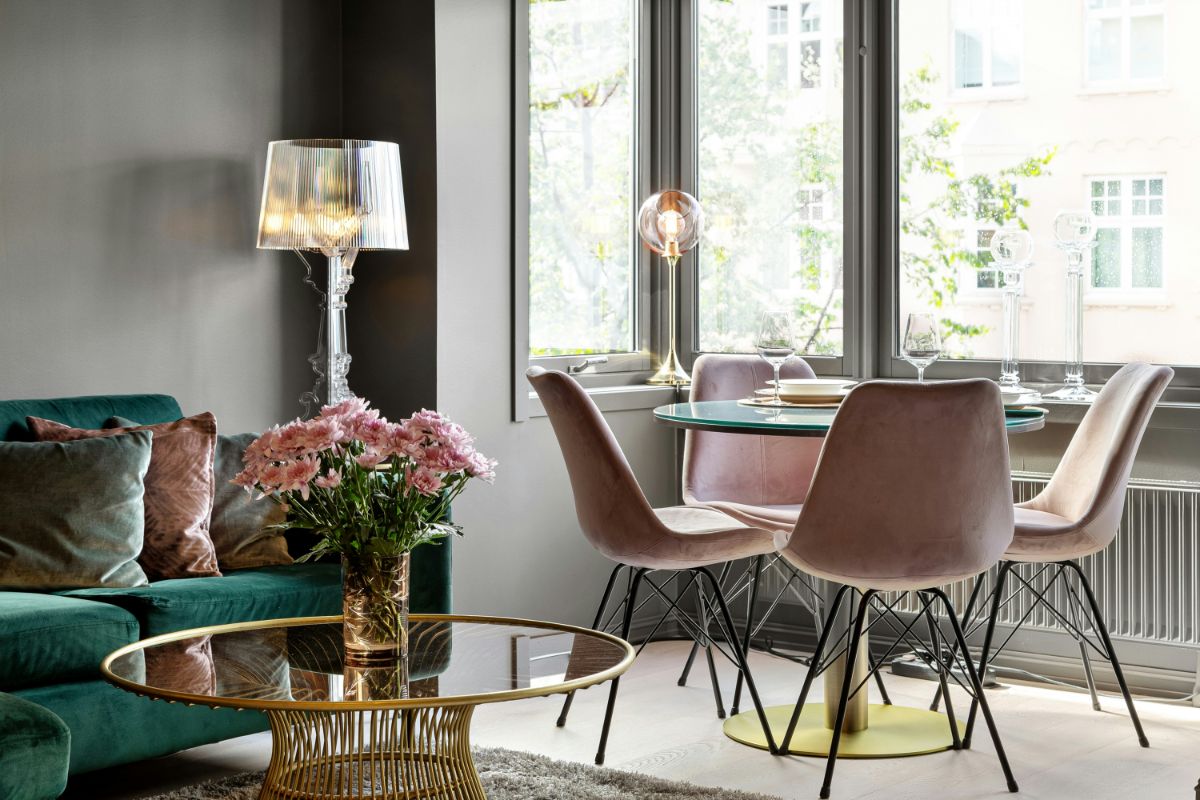 Smaragdovozelená sedačka, staroružové zamatové stoličky, zlatý kovový stolík a dizajnová sklenená stojaca lampa.