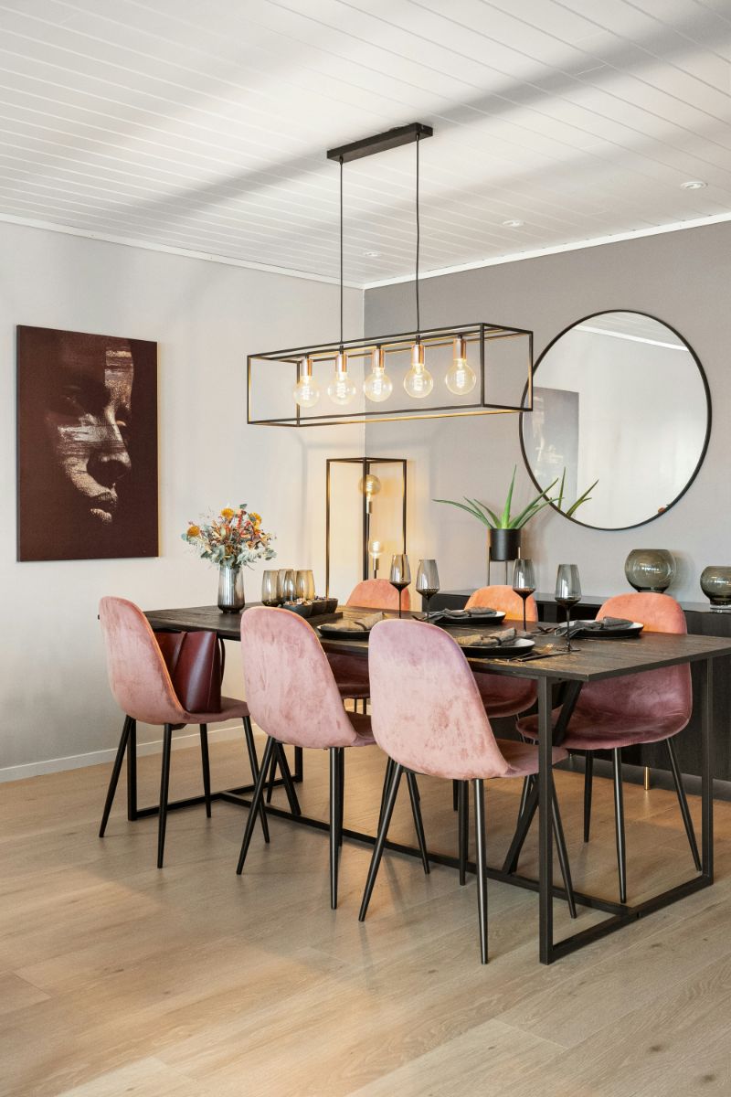 Čierny drevený jedálenský stôl, ružové čalúnené stoličky, lineárne kovové svietidlo a okrúhle nástenné zrkadlo.