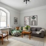 Sivá rohová pohovka, drevený retro nábytok, zelené interiérové doplnky a svetlá drevená podlaha.