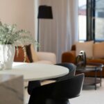 Okrúhly biely stôl, čierne kožené stoličky, škoricové kreslo a biela štruktúrovaná váza.