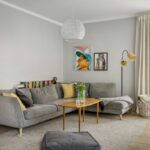 Sivá rohová sedačka, drevený konferenčný stolík, pletený biely kôš a biele steny v škandinávskom interiéri.