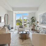 Svetlosivá pohovka, okrúhly kovový stolík, veľký abstraktný obraz a moderná obývacia izba v mestskom štýle.