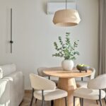 Okrúhly drevený jedálenský stôl, čalúnené béžové stoličky, prútené závesné svietidlo a minimalistický jedálenský kút.