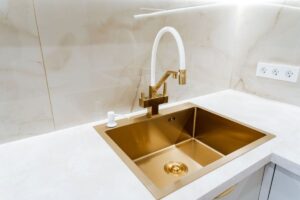 Zlatý kuchynský drez so zlato-bielou batériou na modernej kuchynskej linke.