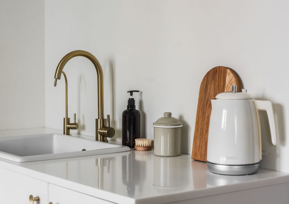 Biela kuchynská pracovná doska s bielym drezom a zlatou batériou.