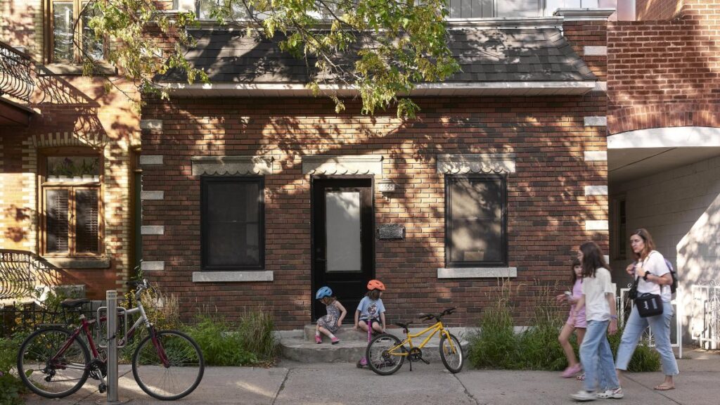 Priečelie tehlového domu s čiernymi okennými rámami, kamennými parapetmi a nízkou dekoratívnou vegetáciou.