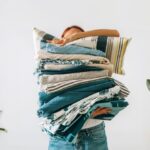 Žena držiaca kopu posteľných obliečok v náručí.