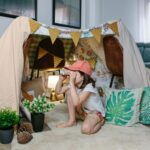 Detský bunker z krémových plachiet, vzorovaných látok a zelených vankúšov s motívom listov na svetlom koberci v obývačke.