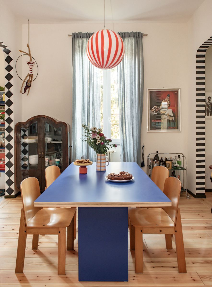 Jedáleň s modrým laminátovým jedálenským stolom, drevenými ohýbanými stoličkami, pruhovaným svietidlom a svetlou drevenou podlahou.