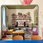 Farebný interiér s červenými policami, žltým kreslom, ružovou pohovkou a čiernobielym pruhovaným lemovaním výrazného prekladu.