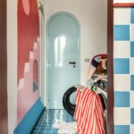 Práčovňa so svetlomodrými oblúkovými dverami, pestrou nástennou maľbou, modrou lesklou dlažbou a práčkou.