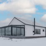 Moderný drevodom s bielou fasádou, sedlovou strechou a presklenou zimnou záhradou.