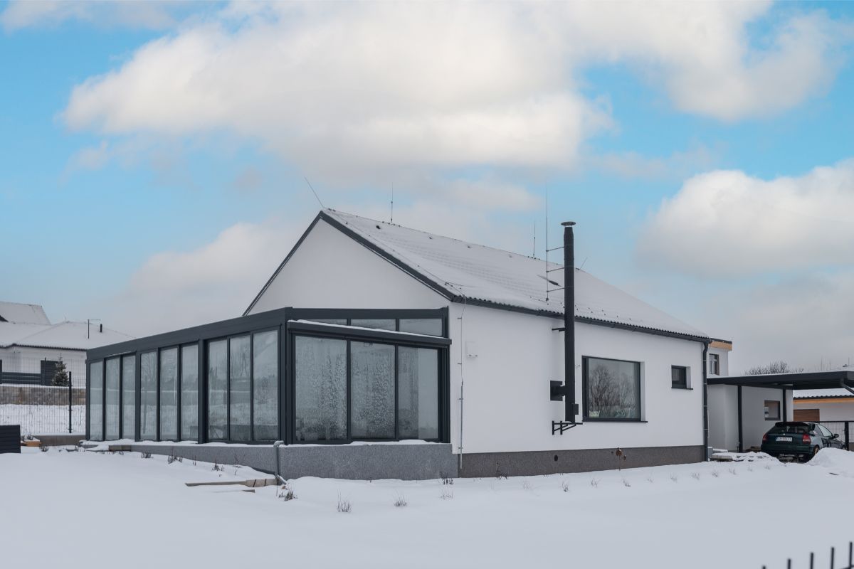 Moderný drevodom s bielou fasádou, sedlovou strechou a presklenou zimnou záhradou.