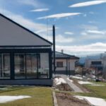 Exteriér domu s presklenou terasou,, vyvýšenými záhonmi a upraveným trávnikom.