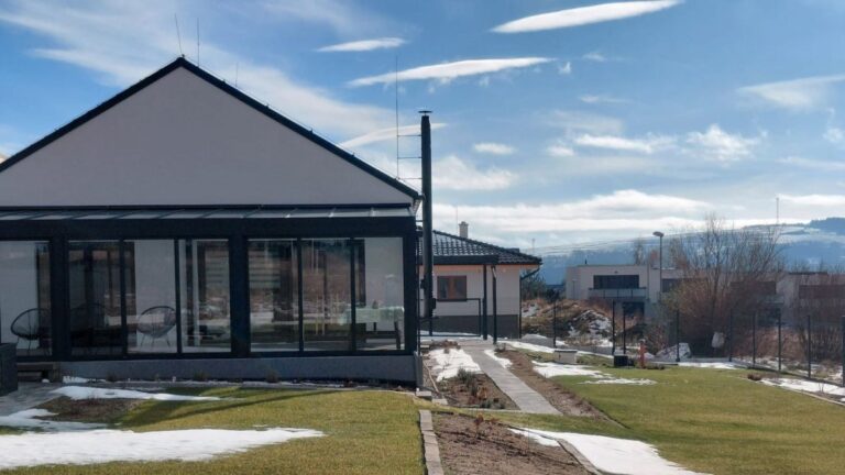 Exteriér domu s presklenou terasou,, vyvýšenými záhonmi a upraveným trávnikom.