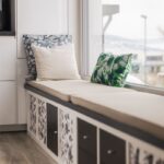 Čalúnená sedacia lavica pod oknom s farebnými vankúšmi a úložným priestorom s kvetinovým vzorom.