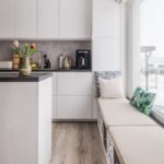 Minimalistická biela kuchynská linka a ostrovček s tmavou pracovnou doskou a moderným kávovarom.