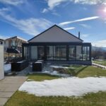 Exteriér domu s presklenou terasou,, vyvýšenými záhonmi a upraveným trávnikom.