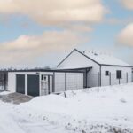 amostatne stojaca dvojgaráž s tmavosivou bránou pri modernom rodinnom dome s bielou fasádou.